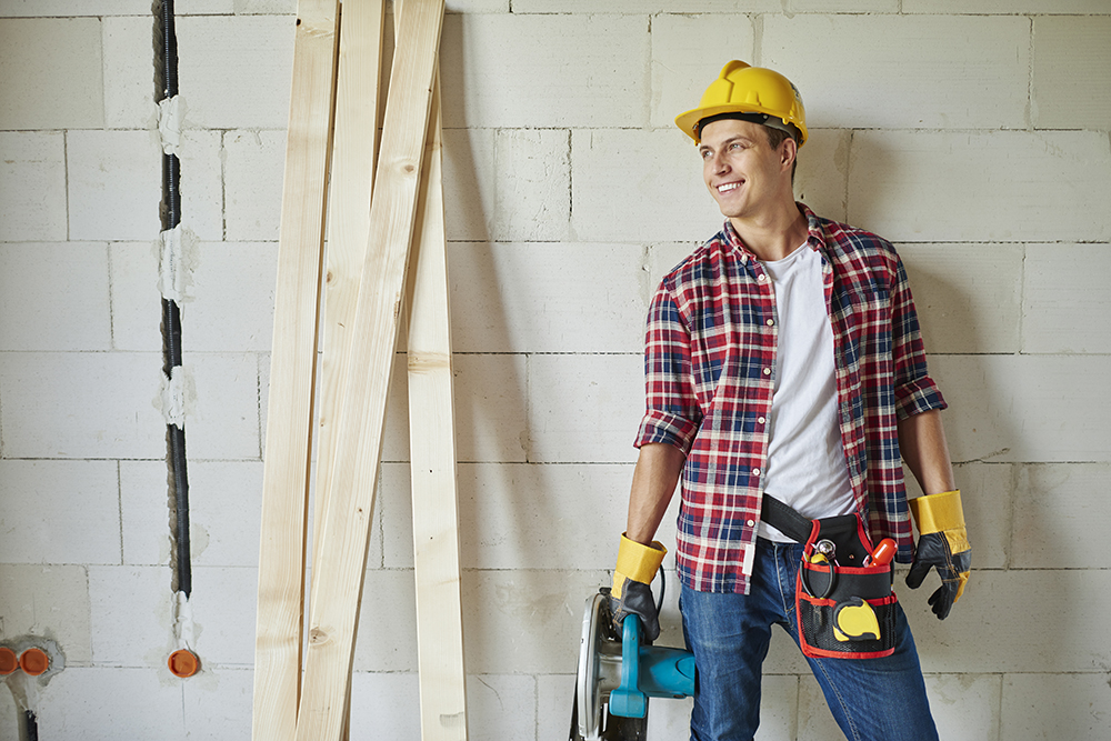Young carpenter is holding electric saw and looking away Young carpenter is holding electric saw and looking away
